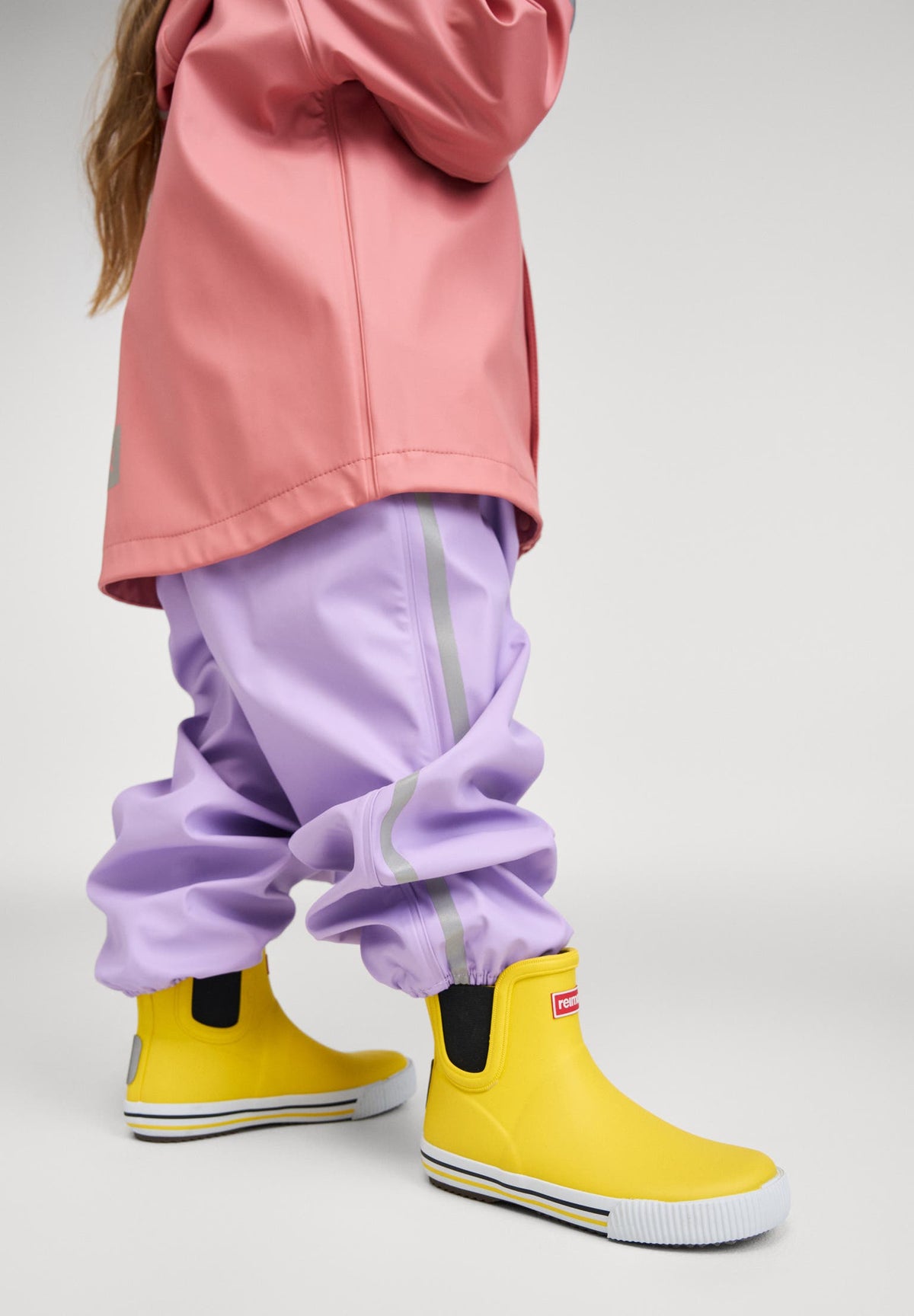 Child playing in shallow water wearing waterproof pink rain jacket and pants — durable kids’ outdoor clothing for spring and summer adventures.