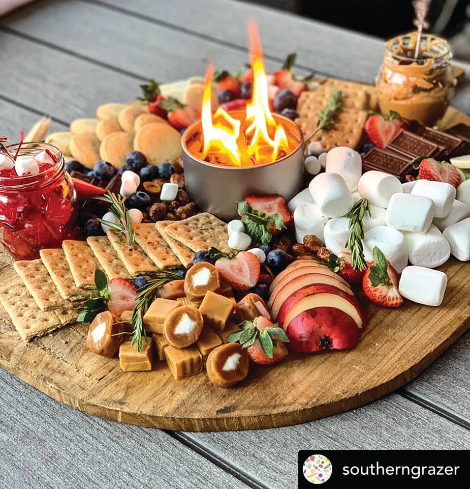 Wooden charcuterie board with food items and a small fire pit, featuring the brand 'southerngrazer'.