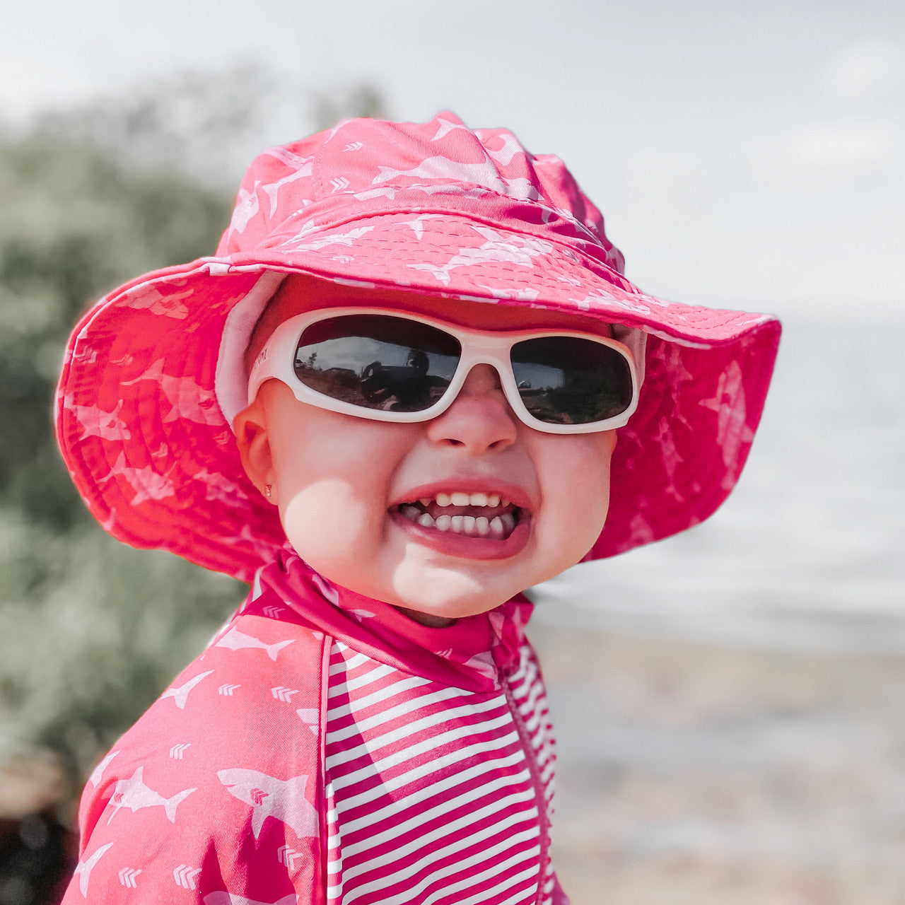 Child wearing a pink sun hat and sunglasses with a blurred background