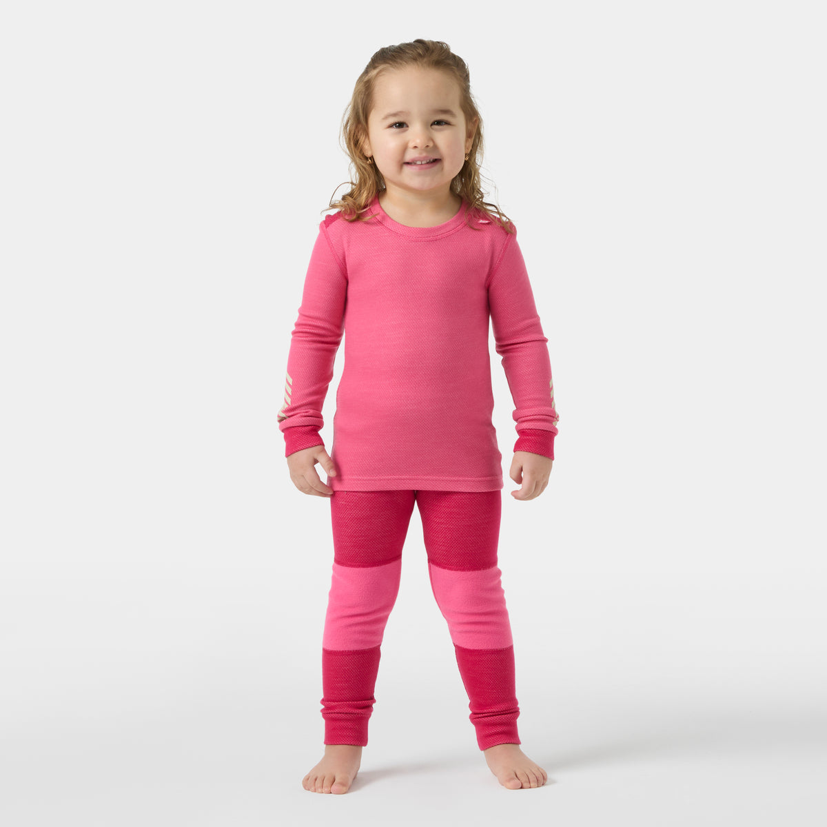 Child standing against a light gray studio background, wearing a bright pink long-sleeve top and matching pink knit pants with darker pink leg sections.