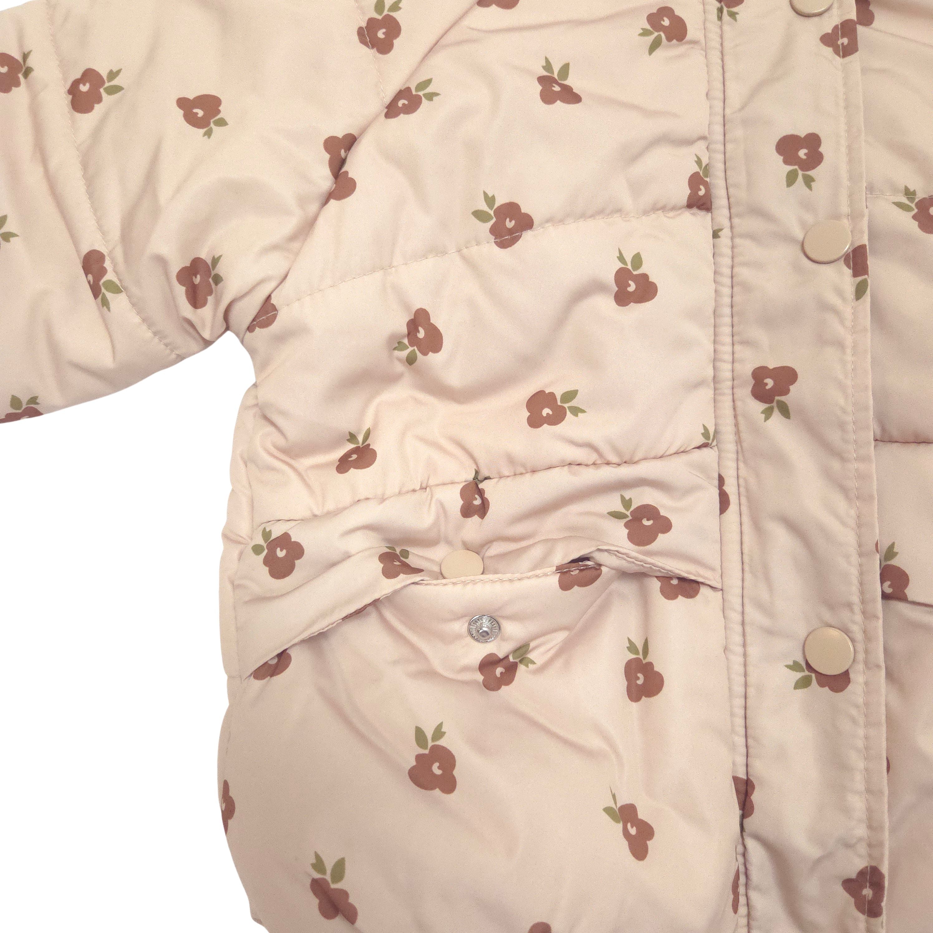 Close-up of a quilted puffer jacket in a light cream color with a small brown floral print and beige snap pocket
