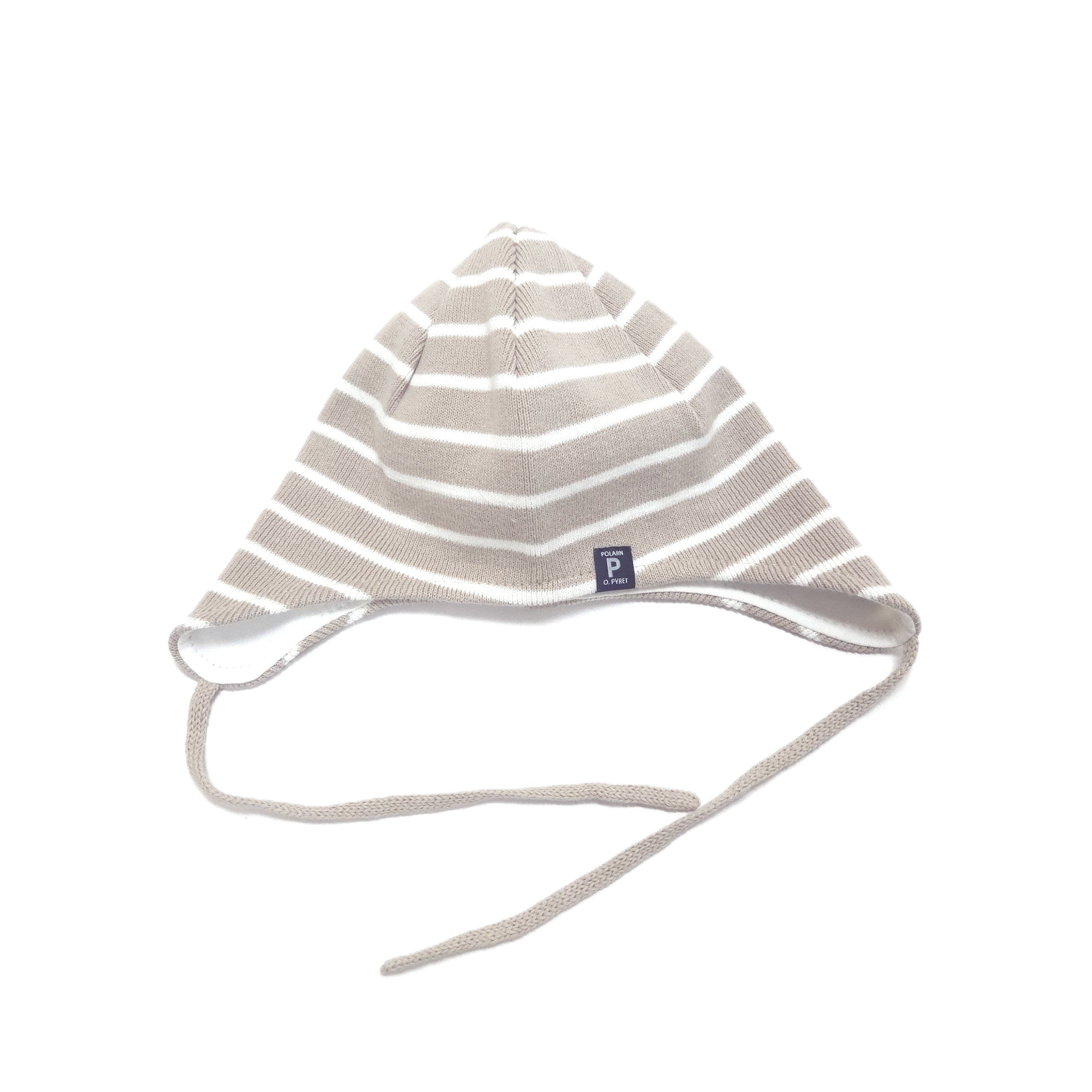 A knit baby bonnet hat with horizontal taupe and white stripes, featuring a small navy blue brand tag and adjustable tie strings, shown on a plain white background.