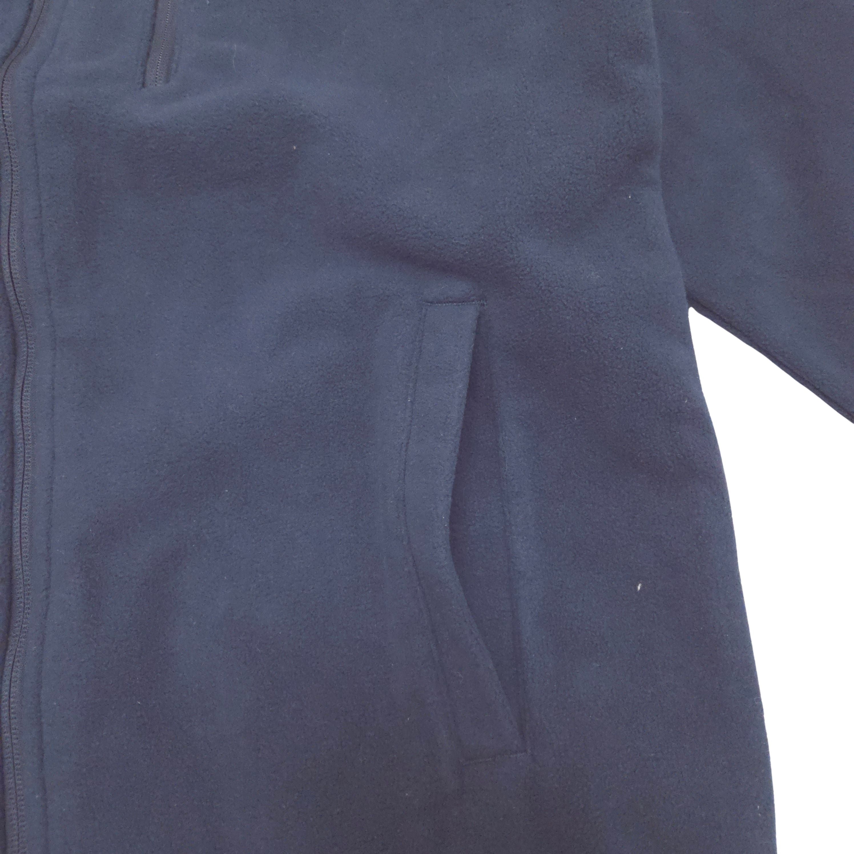Close-up of a dark navy blue fleece jacket showing a side pocket and zipper detail against a white background.