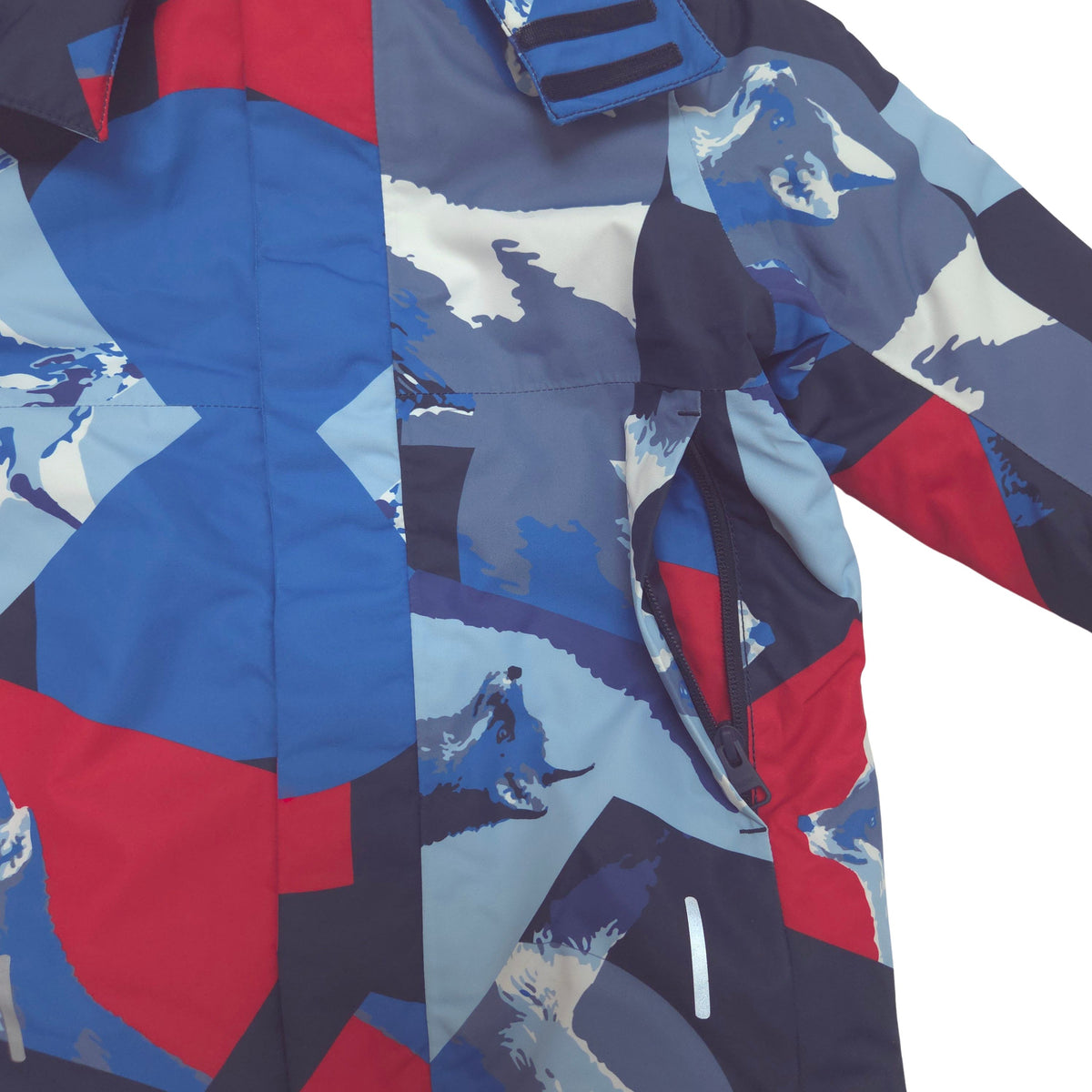 A close-up of a winter jacket featuring a bold geometric and abstract pattern in blue, red, navy, and light gray, with a visible zipper pocket.