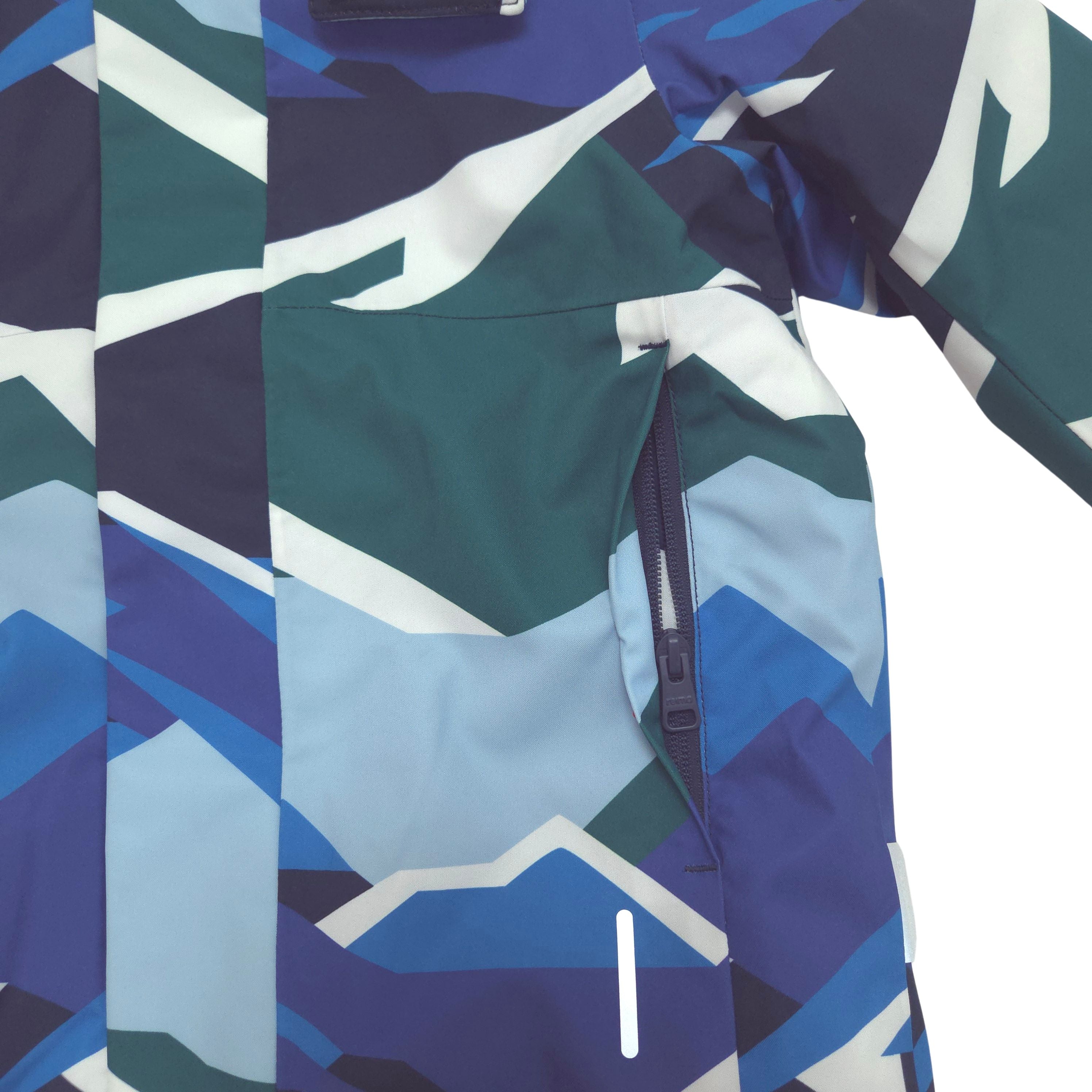Close-up of a technical outdoor jacket featuring a geometric mountain pattern in shades of blue, teal, navy, and white, with a visible front zippered pocket