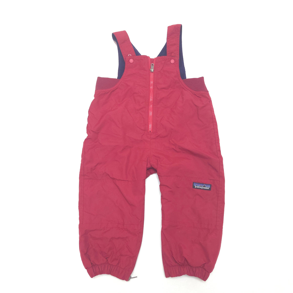 A pair of Patagonia children's snow bib overalls in a red color, featuring a front zipper, elastic cuffs, and a small Patagonia logo patch on the left leg, laid flat on a white background.