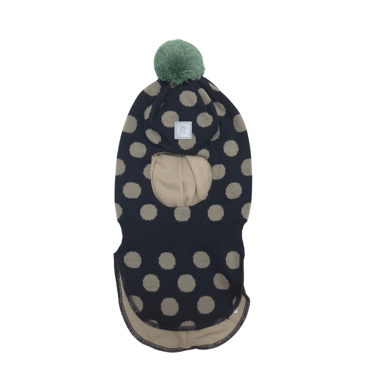 A knit balaclava with a black and beige polka dot pattern, featuring a beige face opening, a beige inner lining, and a green pom-pom on top.