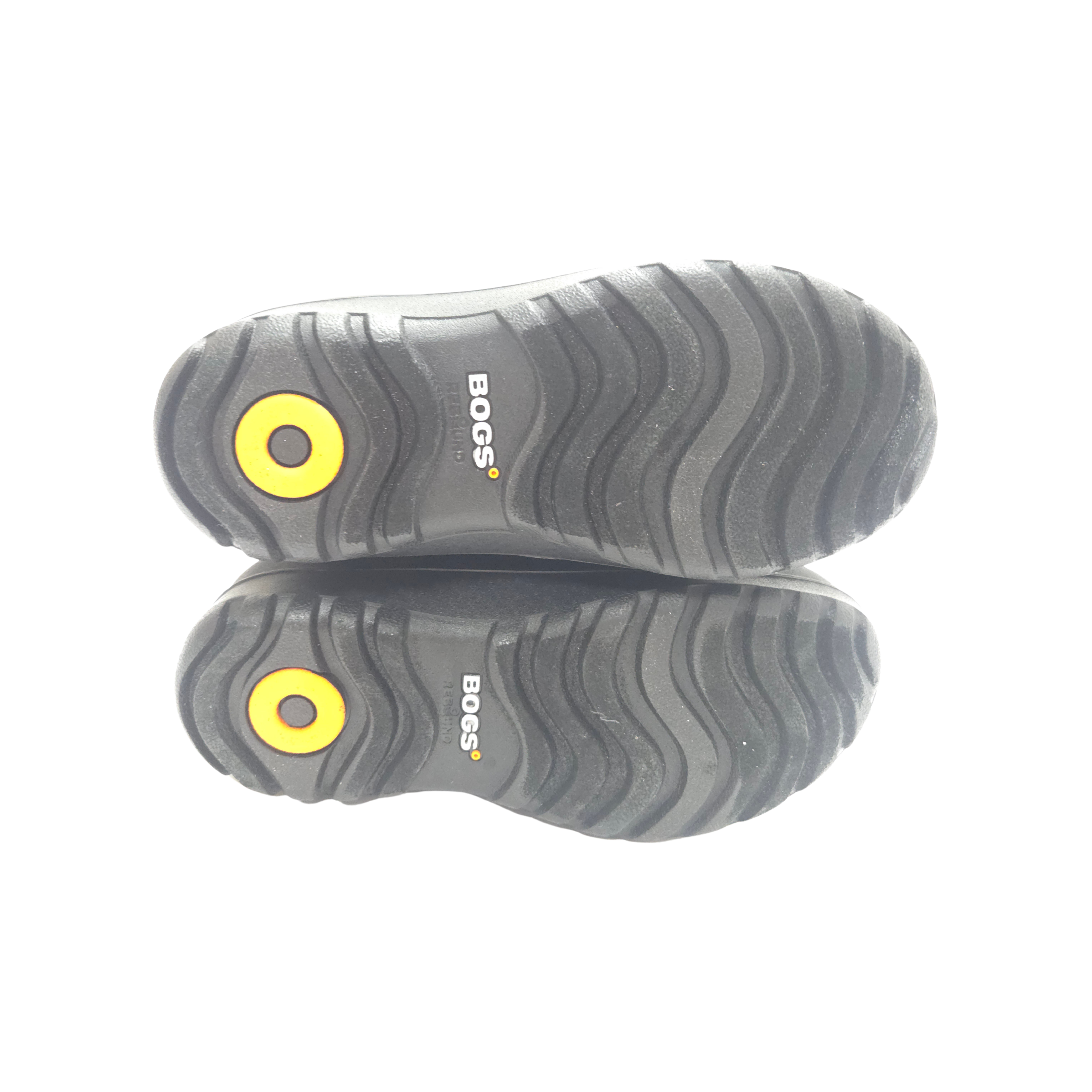 A pair of black BOGS boots shown from the sole view, featuring a textured black rubber tread with a bright yellow circular logo accent and white BOGS branding.