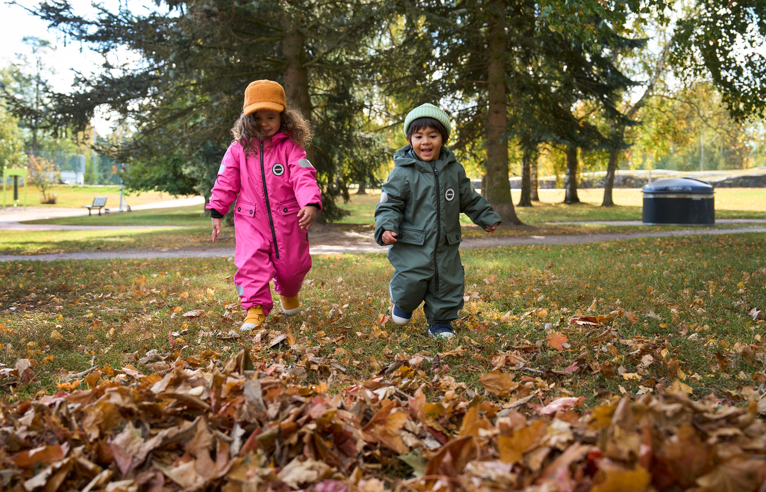 Two children playing in a park with fallen leaves, wearing colorful winter outfits.