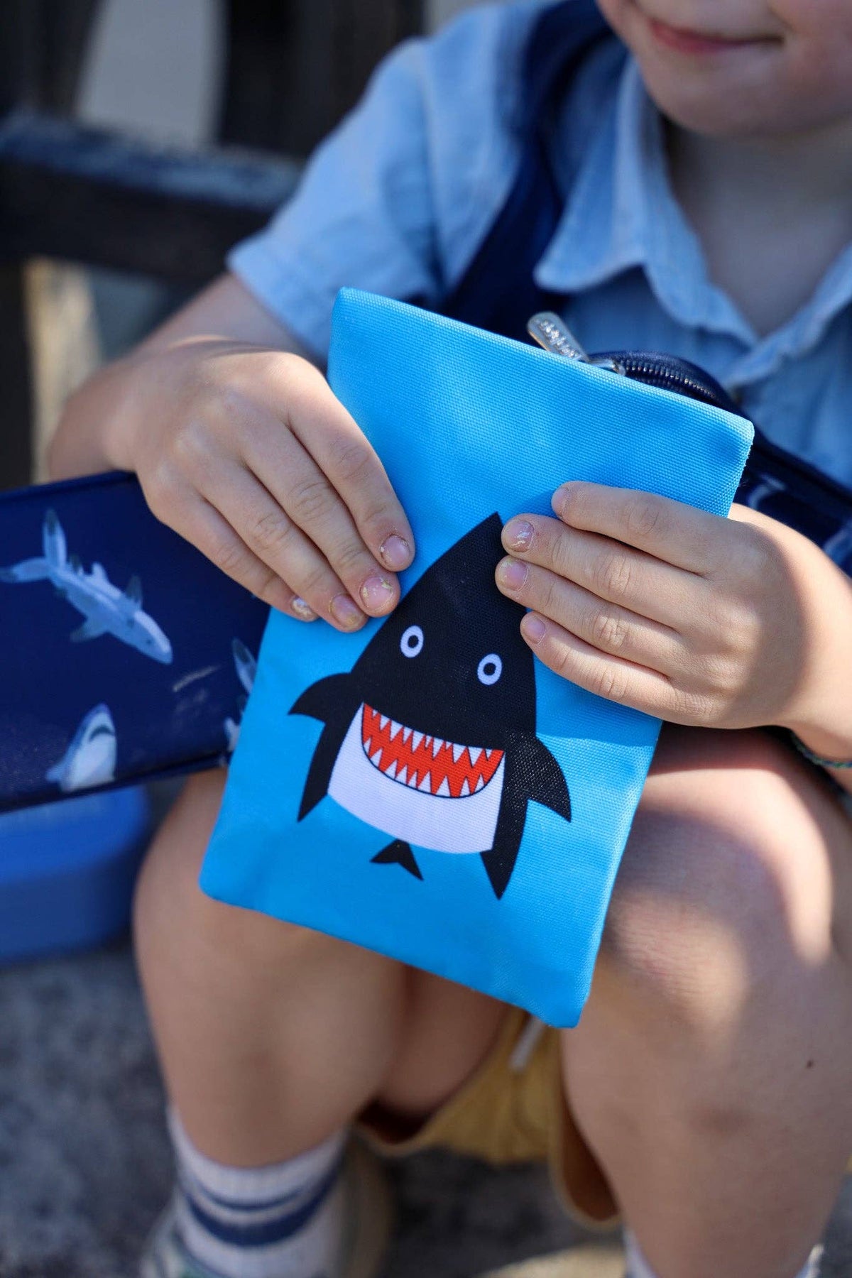 Child holding a blue pouch with a shark design