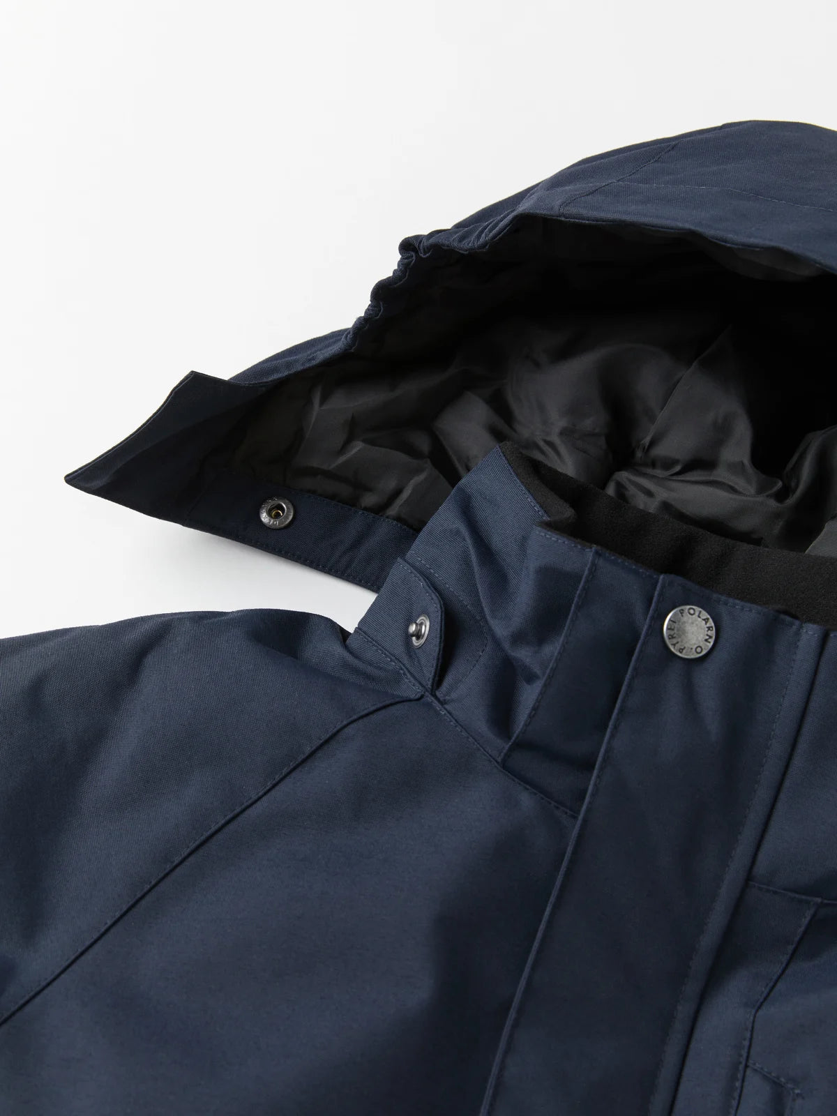 Close-up of a navy blue hooded Polarn O. Pyret witer jacket with a black inner lining and silver snap buttons, shown on a clean white background. Image focuses on detachable hood.