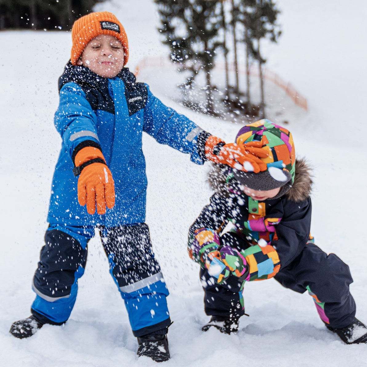 Smiling child in a blue winter jacket and knit hat holding a red cup outdoors in the snow — cozy winter adventure with kids’ outdoor gear