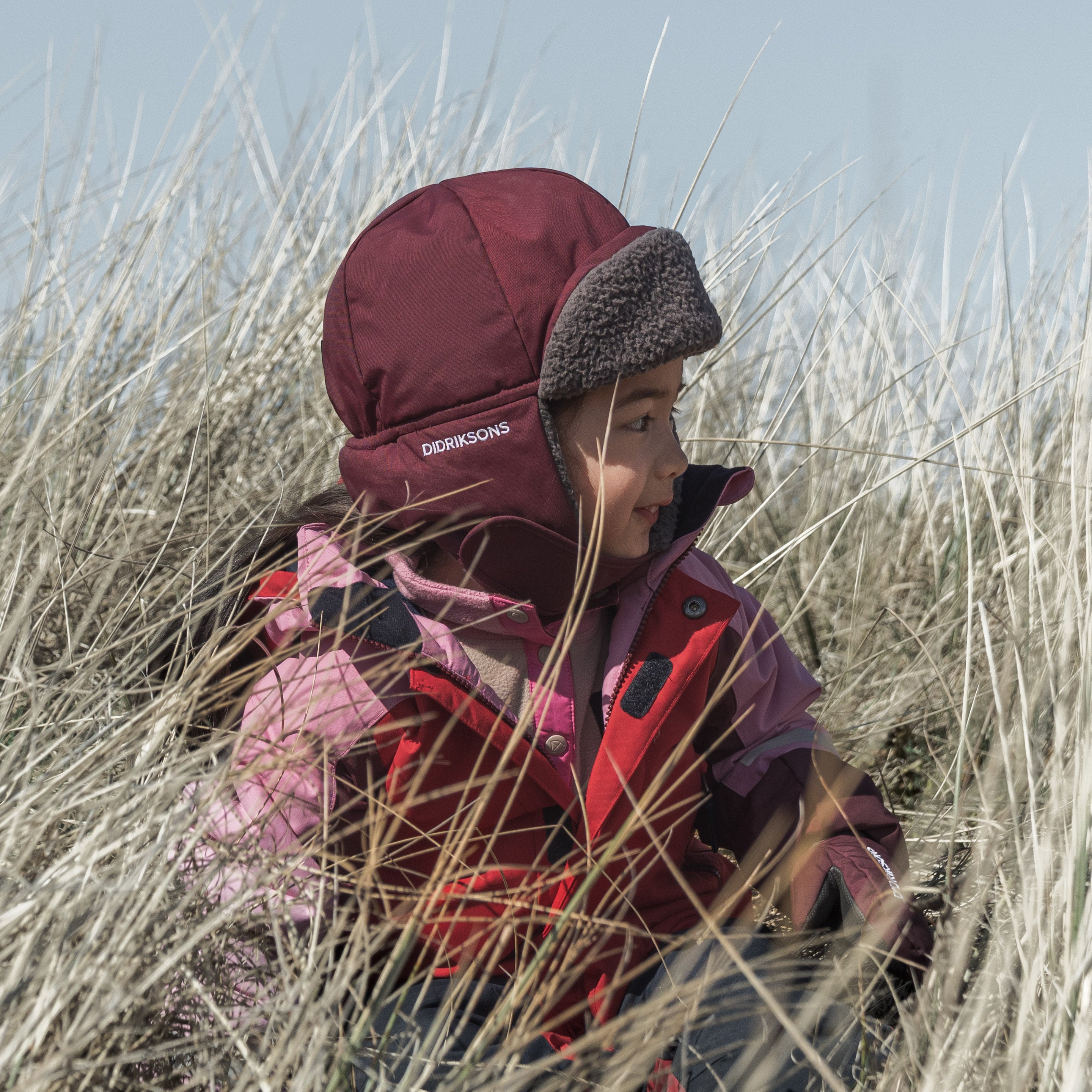 Child dressed in Didriksons winter gear exploring tall grass dunes on a cold, sunny day