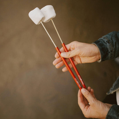 Person holding red marshmallow sticks with marshmallows against a brown background