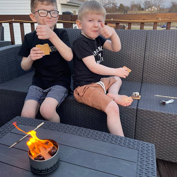 Two children sitting on a patio with a small fire pit in front of them.