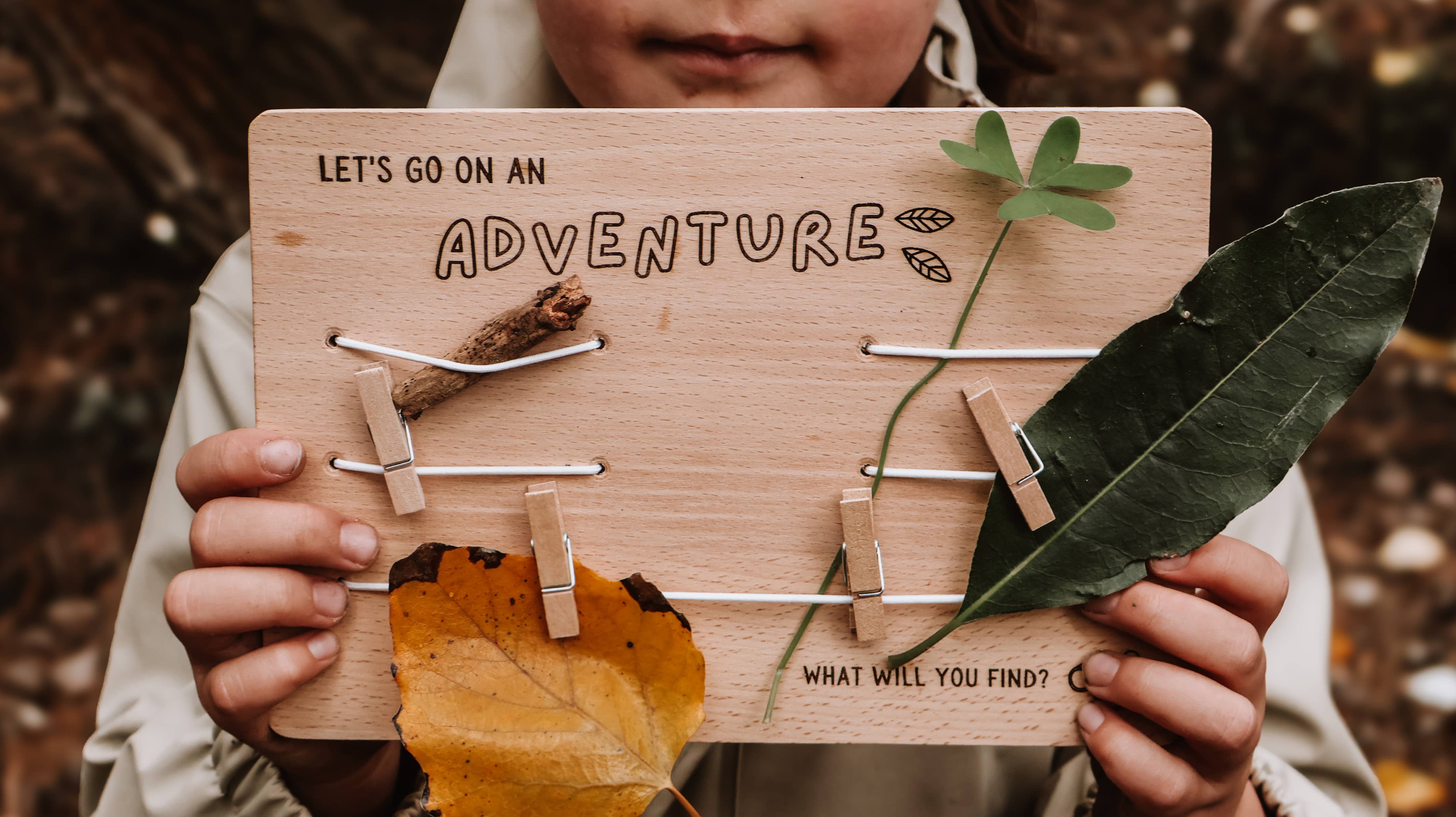Person holding a wooden board with 'Let's go on an adventure' text and leaves.