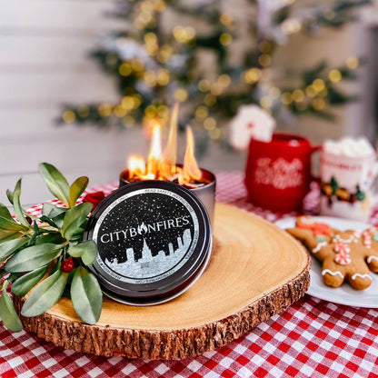 Candle with 'City Bonfires' branding on a wooden coaster with Christmas decorations in the background.
