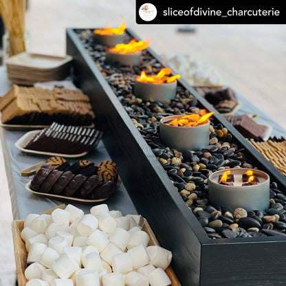 Outdoor charcuterie board with candles and marshmallows on a stone surface.