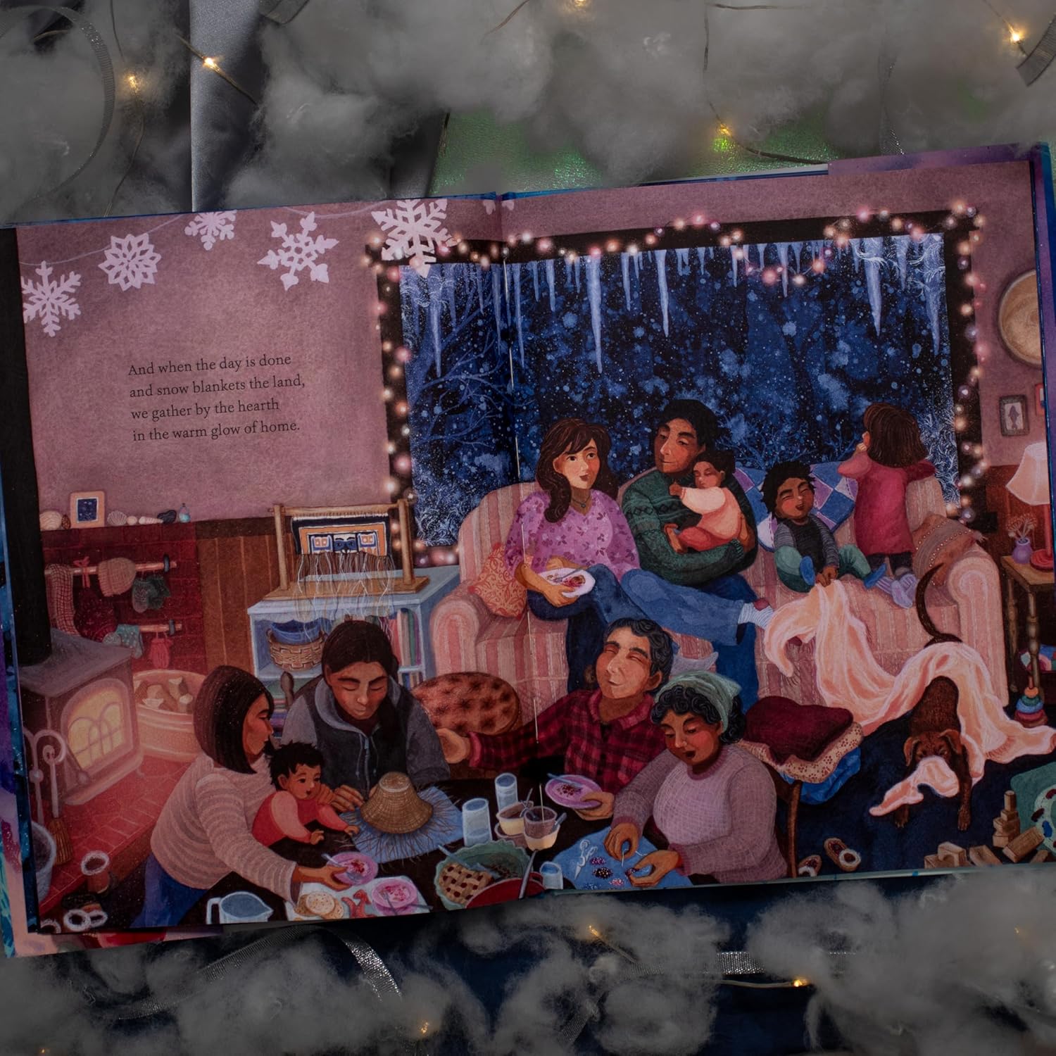 Illustrated book open to a page with a family gathered around a table, surrounded by snowflakes and lights.
