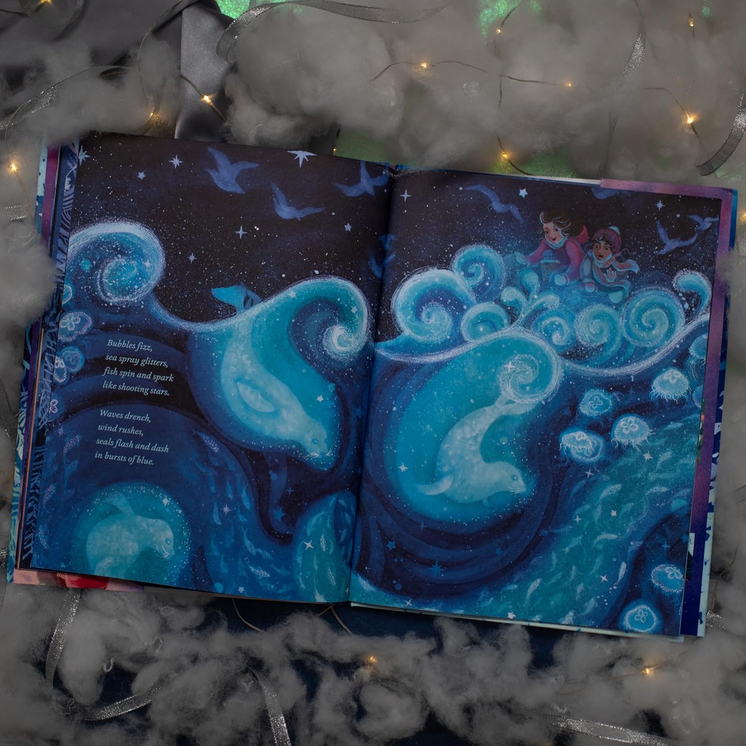 Open book with mermaid and dolphin illustration on a textured surface with lights.