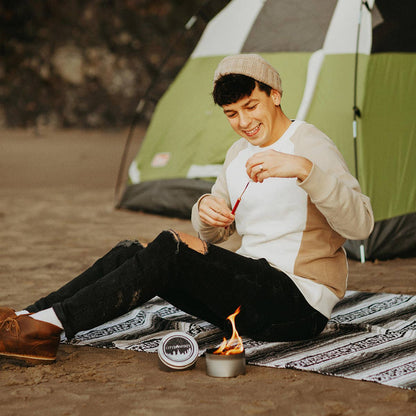 Man sitting by a campfire with a tent in the background