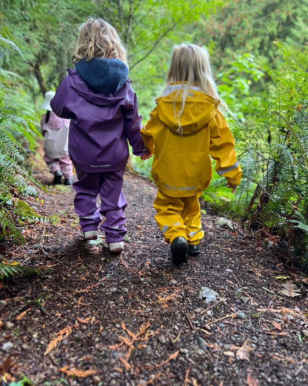 Two children in raincoats walking on a forest path