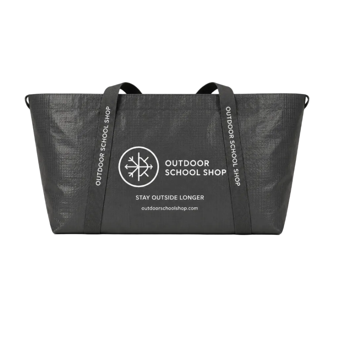 Black tote bag with 'Outdoor School Shop' branding and measurements on a beige background