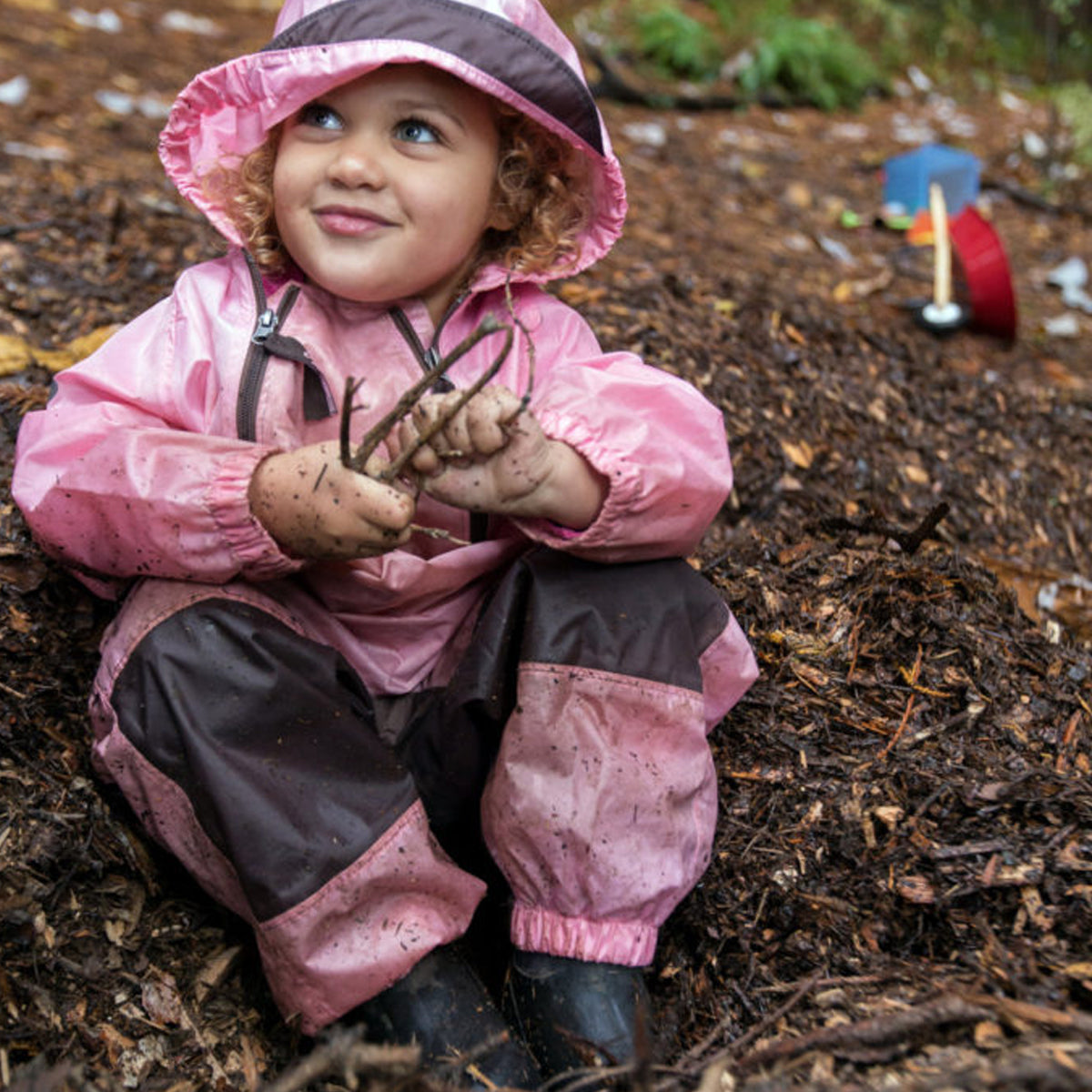 Child in pink raincoat holding sticks in a forest setting