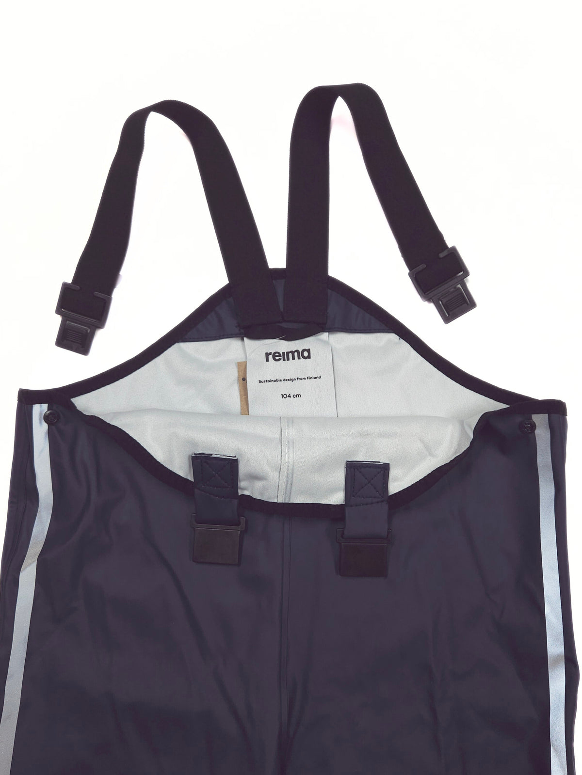 Close-up of a Reima waterproof bib , showing the dark navy exterior, adjustable black shoulder straps with plastic buckles, a white inner lining, and reflective silver side stripes.