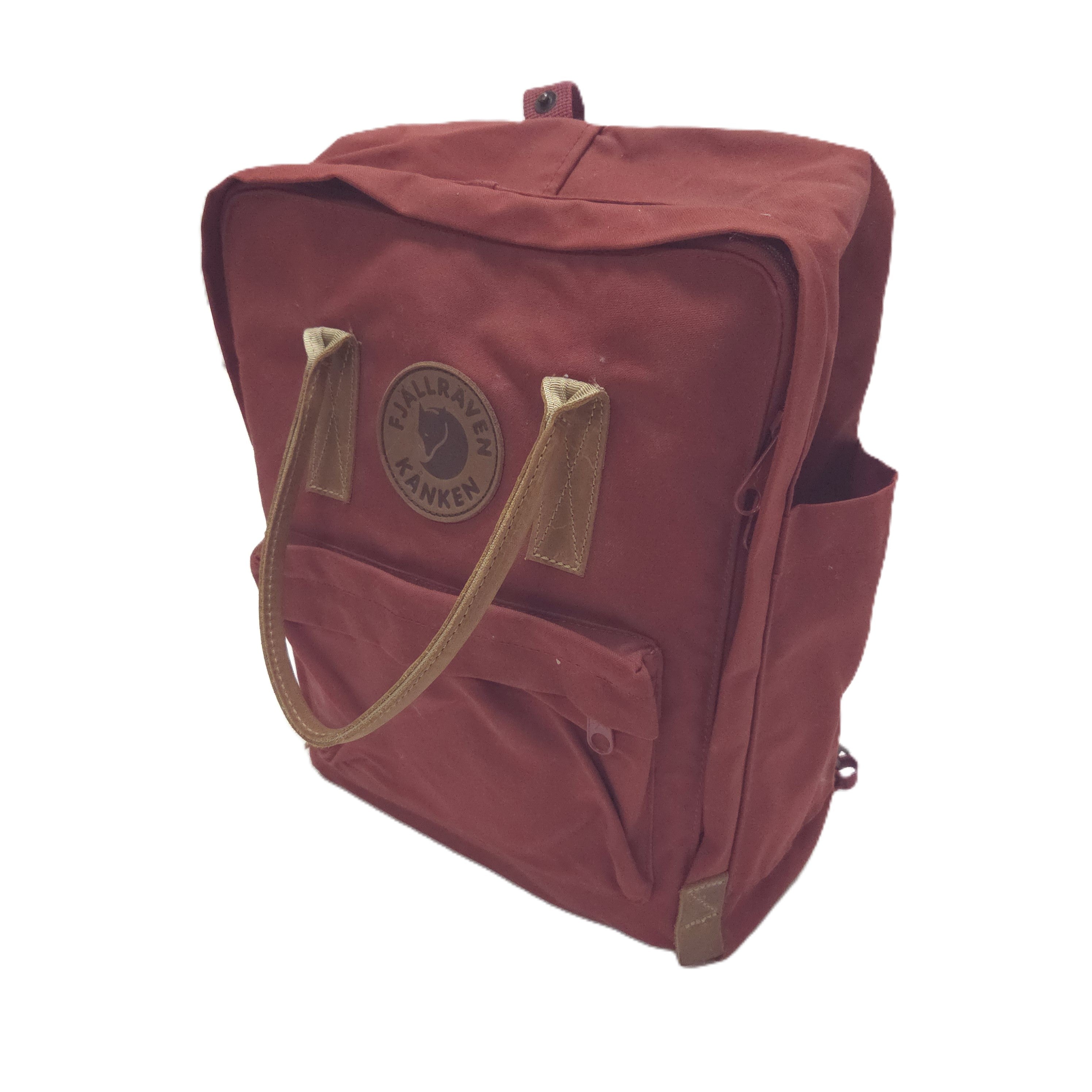 A Fjälör red canvas backpack with tan leather handles and a circular brown logo patch on the front pocket, shown against a plain white background.