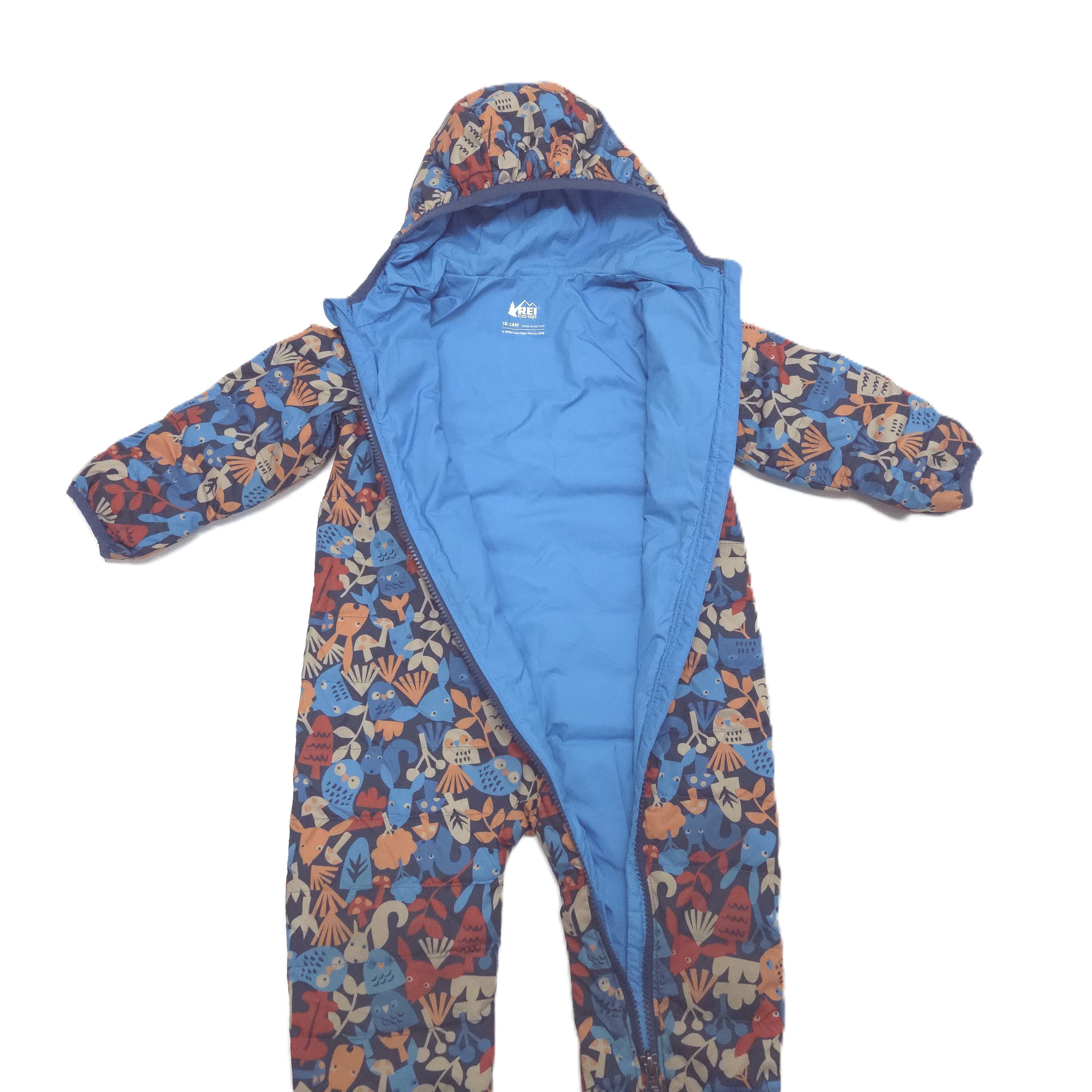 A hooded one-piece baby puffersuit with a blue interior and a multicolor tropical print on the exterior. The print features blue, orange, and beige tropical motifs.