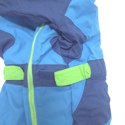 Close-up of a blue and navy winter jacket with bright neon green zipper and hook-and-loop strap details, shown on a white background.