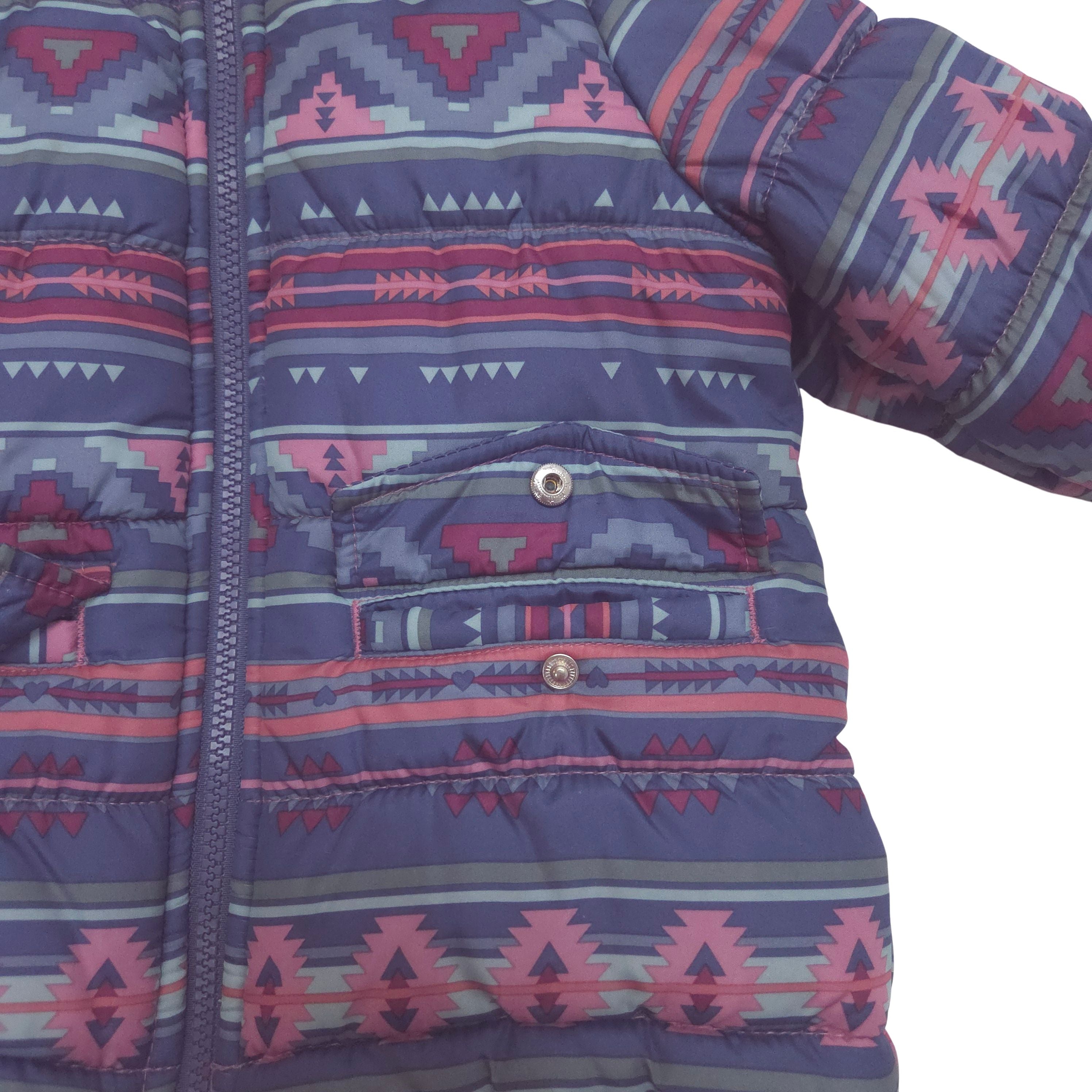 A close-up of a children's puffer jacket featuring a purple, pink, and gray geometric Southwestern pattern, with a front zipper and a buttoned waist pocket.