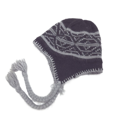 A black knit winter hat with ear flaps and braided tassel ear ties, featuring a light gray geometric pattern across the crown.
