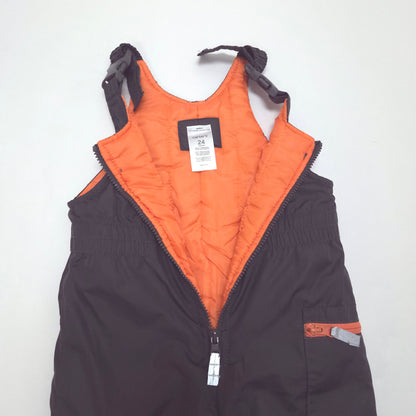 A black insulated bib-style snow pants with a bright orange quilted interior lining, laid flat on a white background. The zipper is open, showing the interior details, straps, and a brand label.