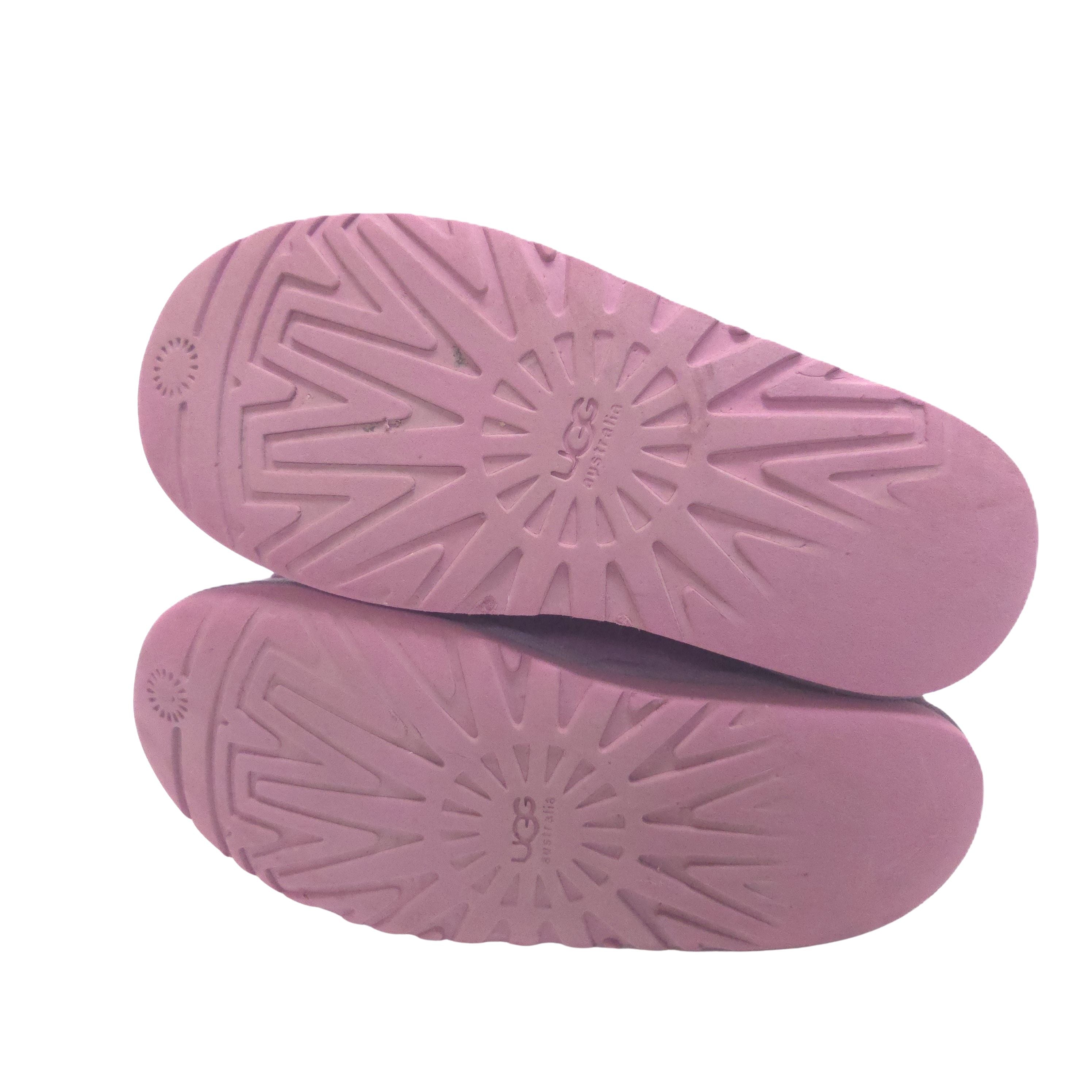 A pair of pink UGG slip-on boots shown from the sole side, featuring a textured radial tread pattern and the embossed UGG logo in the center.