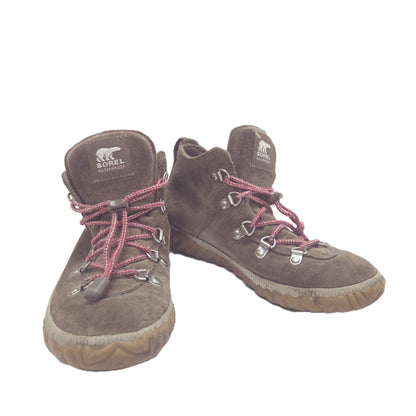 A pair of brown suede boots with red braided laces and silver metal eyelets, shown against a plain white background.