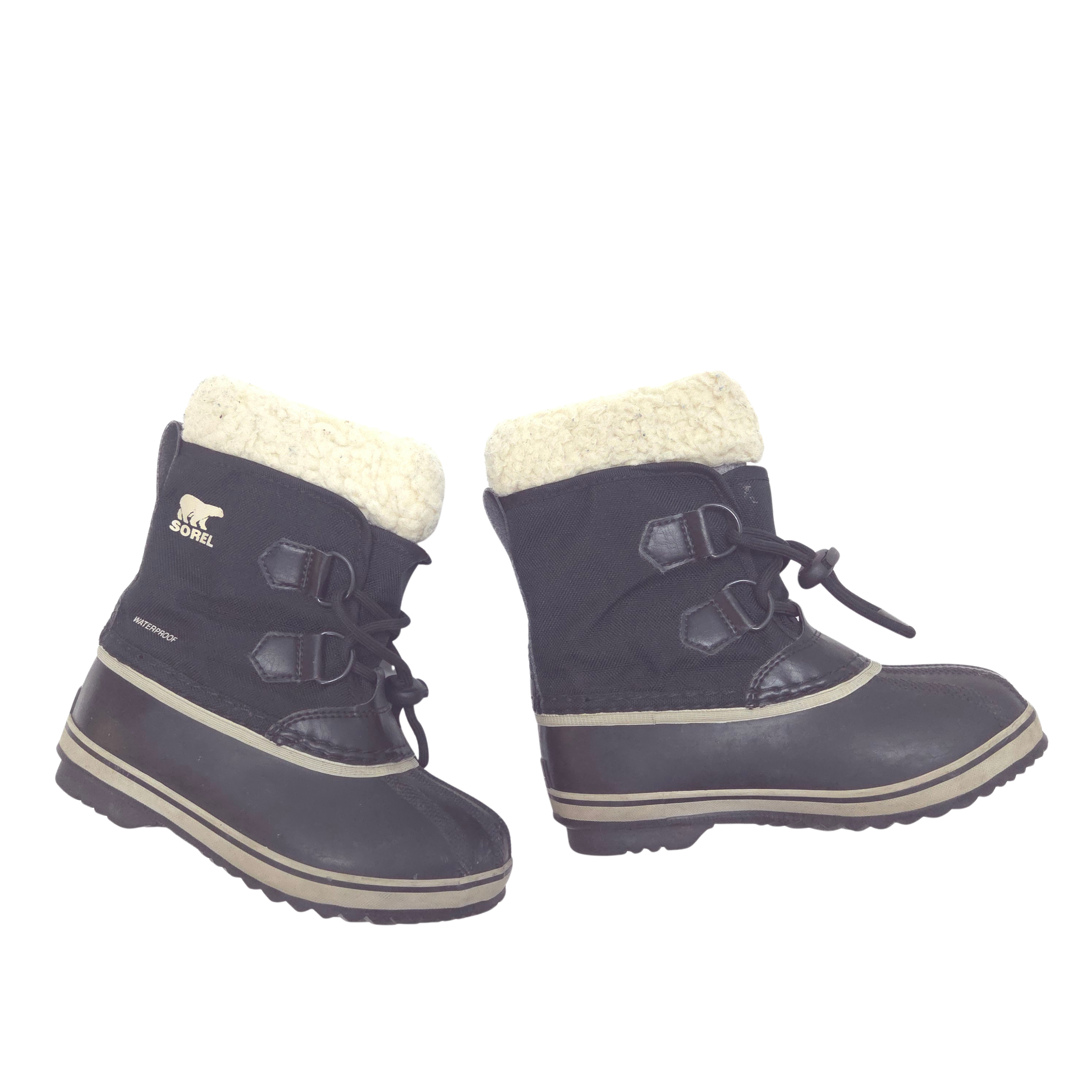 A pair of Sorel children's winter boots in black with a cream sherpa lining and beige trim, shown against a plain white background.