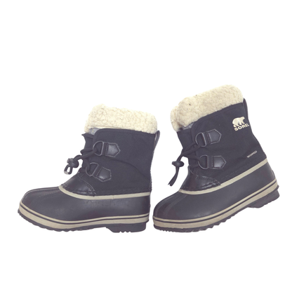 A pair of Sorel kids' winter boots in black with a cream sherpa lining and beige trim, shown against a plain white background.
