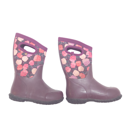 A pair of children's rain boots in a muted plum purple color, featuring a floral print pattern on the upper shaft with pink, red, and peach roses on a dark background.