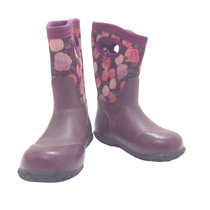 A pair of children's rain boots in a dark plum purple color, featuring a floral pattern on the upper shaft with pink and red roses, set against a plain white background.