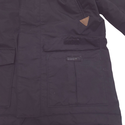 Close-up of a black quilted jacket with a front flap pocket, a hook-and-loop closure, and a small brown triangular leather accent near the chest.
