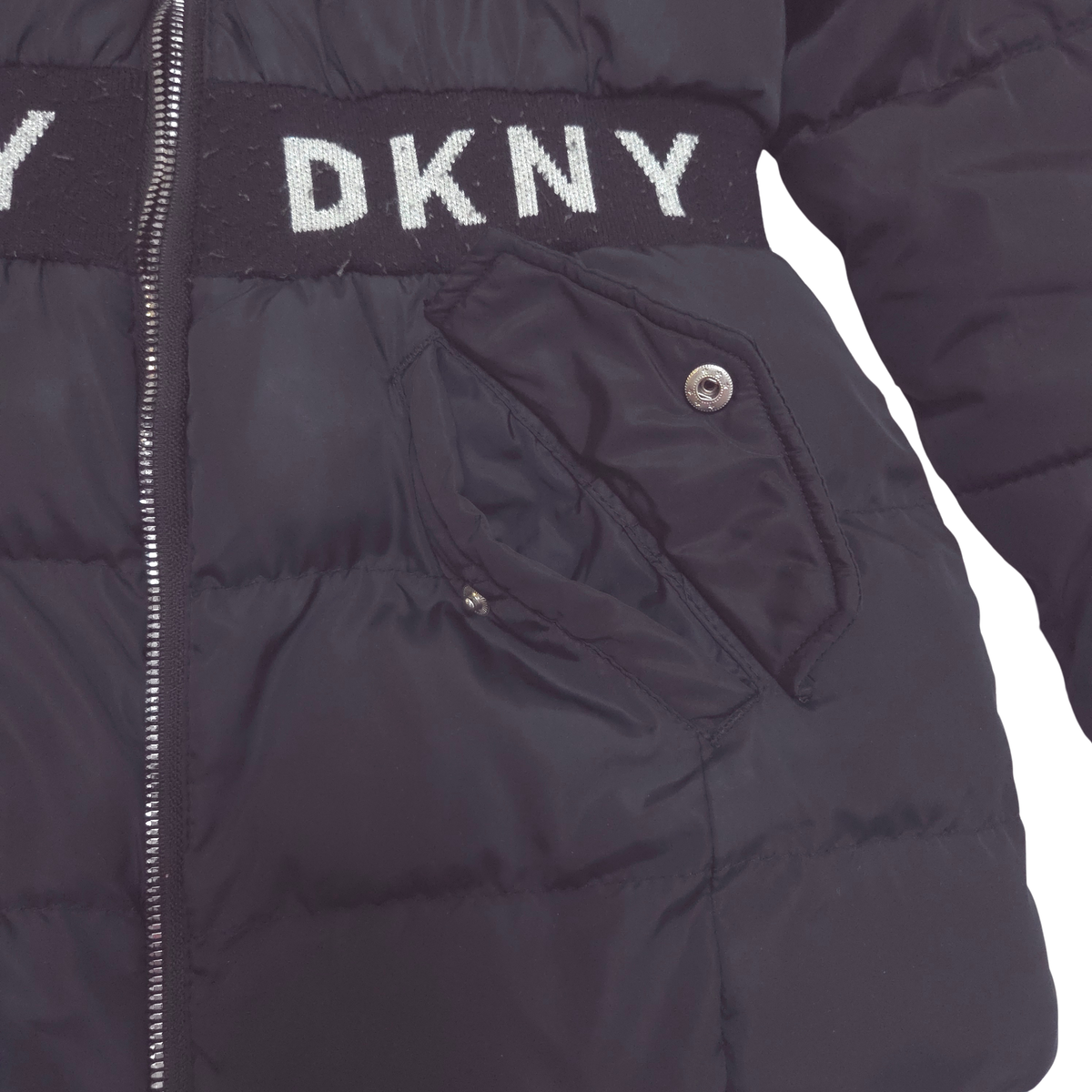 Close-up of a black puffer jacket with a wide black waistband featuring the white DKNY logo and a side pocket with a snap closure.
