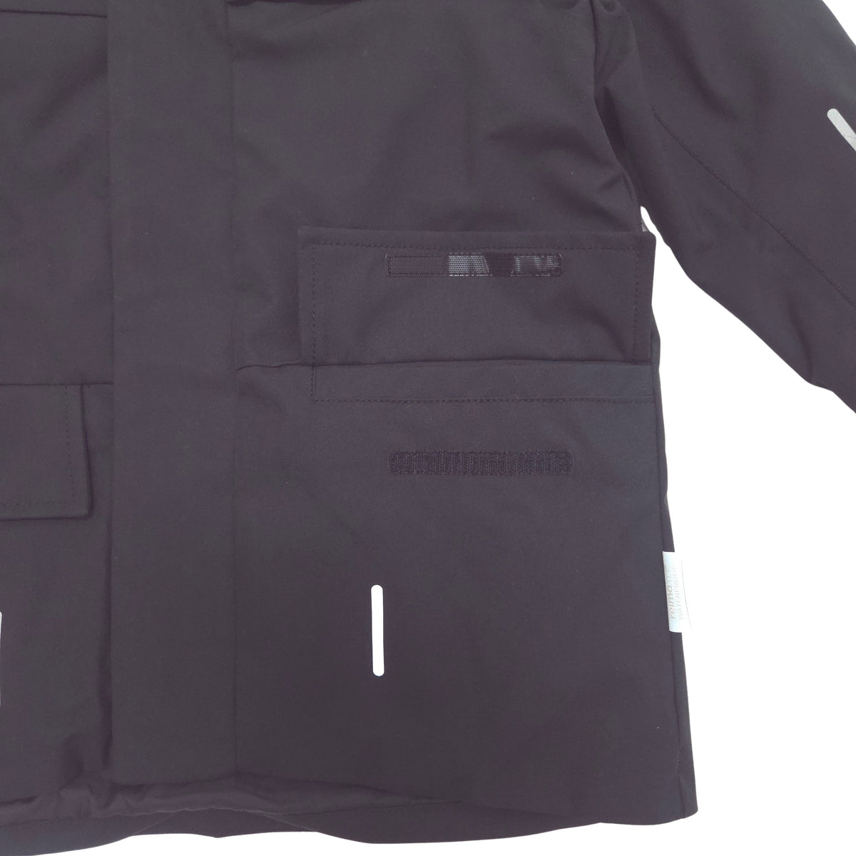 Close-up of a black winter jacket with a front flap pocket, reflective white vertical striping, and a small white brand tab on the sleeve.
