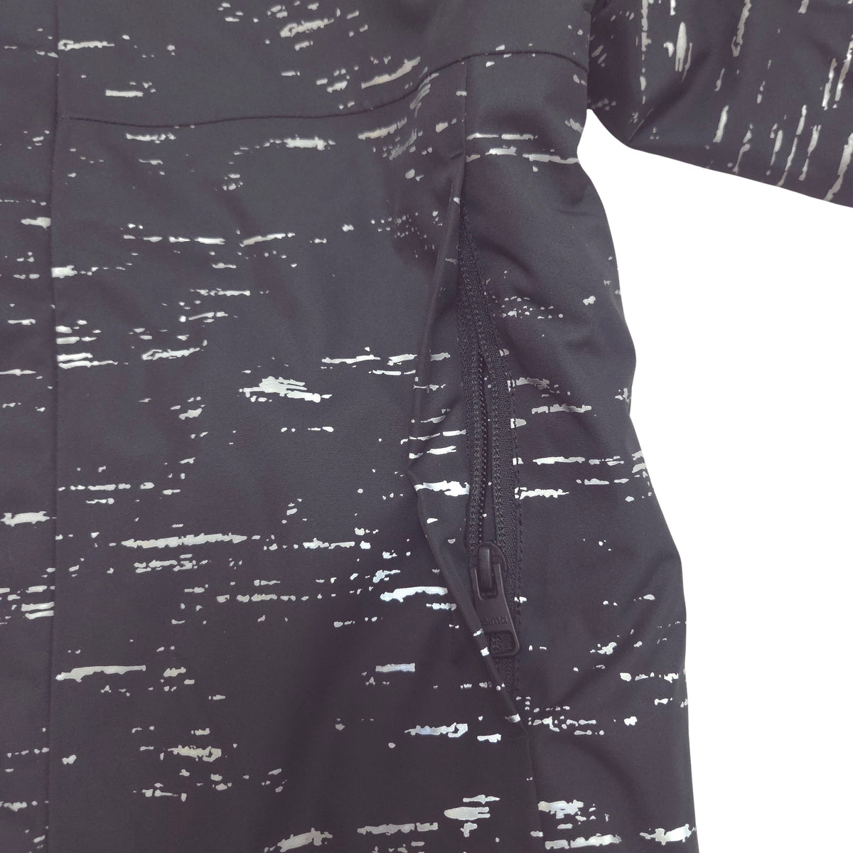 Close-up of a dark gray or black jacket with a white distressed, paint-splatter pattern and a side zipper hand pocket.