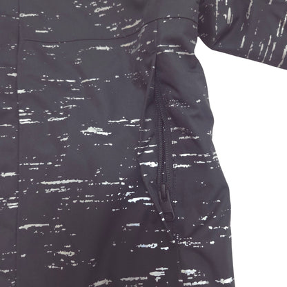 Close-up of a dark gray or black jacket with a white distressed, paint-splatter pattern and a side zipper hand pocket.