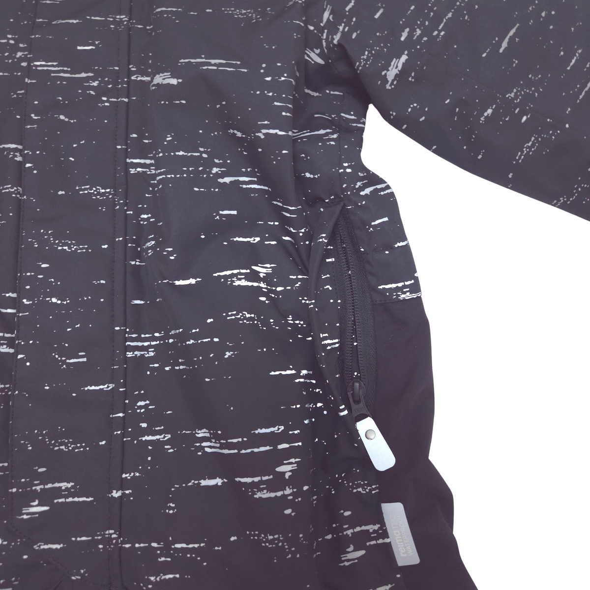 Close-up of a dark jacket sleeve and torso showing a black and white speckled pattern, a zippered pocket, and a white zipper pull on a white background.