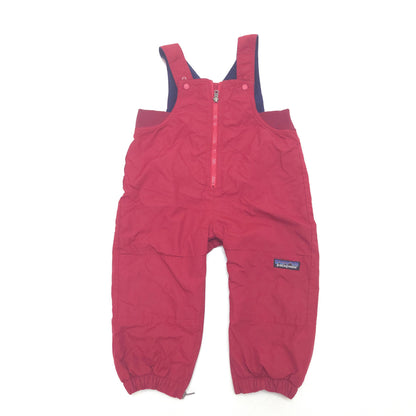 A pair of Patagonia children's snow bib overalls in a red color, featuring a front zipper, elastic cuffs, and a small Patagonia logo patch on the left leg, laid flat on a white background.