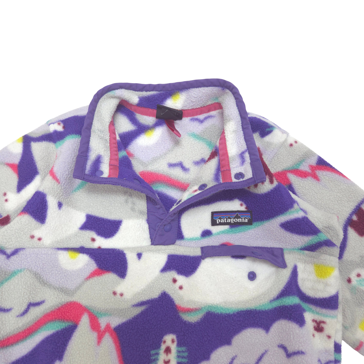 Close-up of a Patagonia fleece pullover with a purple collar and a multicolor abstract pattern on a white background. small chest pocket