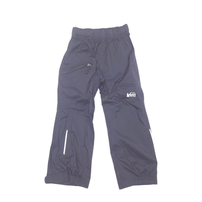 Black outdoor shell pants with an elastic waistband, zippered pockets, and a small white logo on the left thigh, shown against a plain white background.